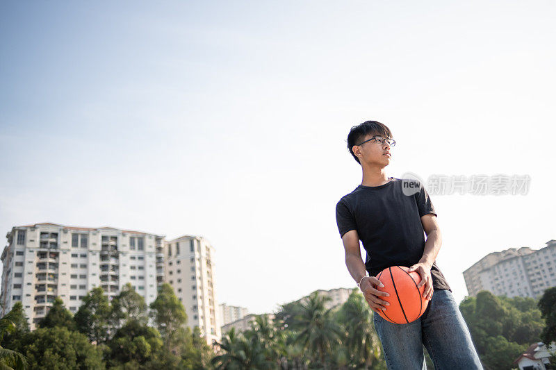 asian chinese teenage boy holding his basket ball and looking away